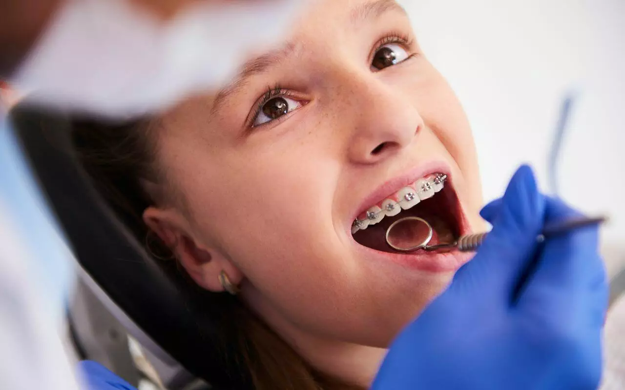 A young girl with braces is getting her teeth checked by a dentist.