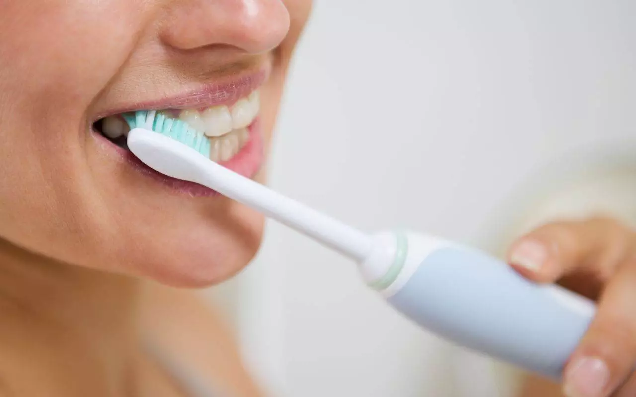 A woman is brushing her teeth with an electric toothbrush.